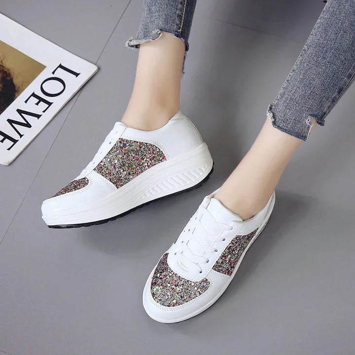 White platform sneakers with multicolor glitter panels worn with ripped skinny jeans on gray floor