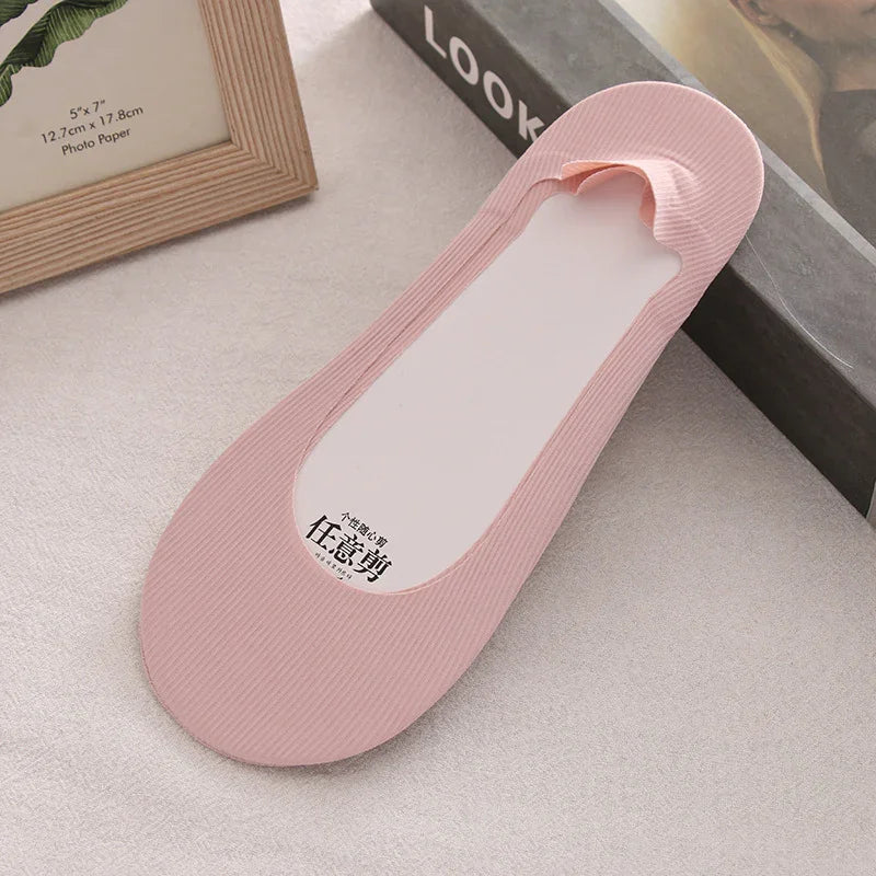 Light pink no-show foot liner sock on beige surface with photo frame and book background