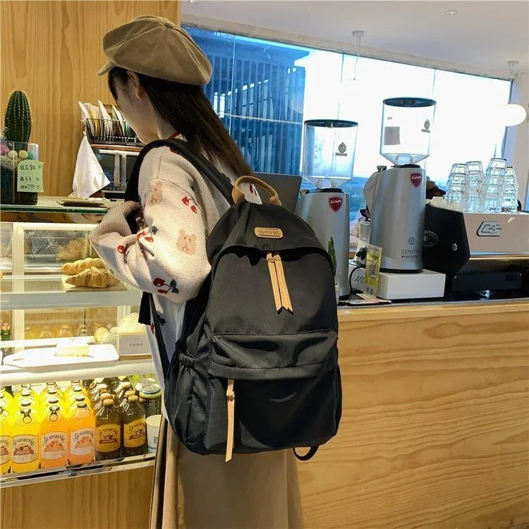Woman wearing beige beret and floral sweater with black backpack in modern cafe near pastry display and espresso machines