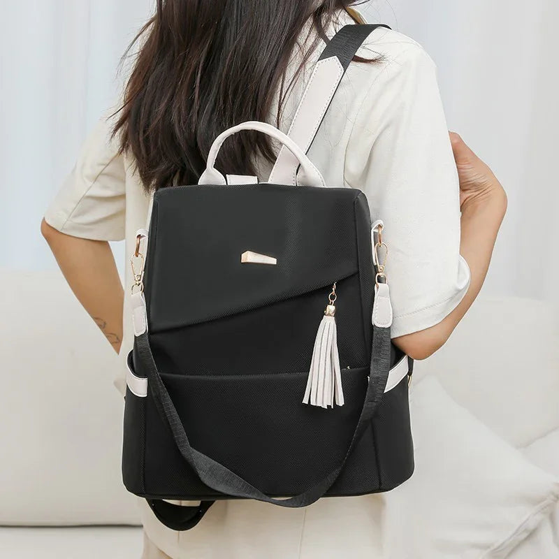 Black and white women's backpack with tassel detail worn by a person in beige outfit