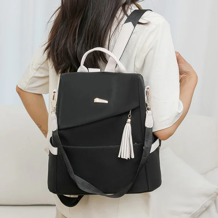 Black and white women's backpack with tassel detail worn by a person in beige outfit