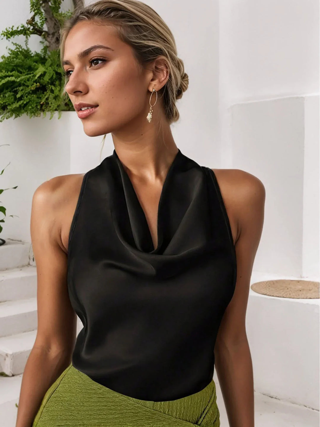 Woman wearing black satin halter top and green textured skirt in minimal white interior with plants