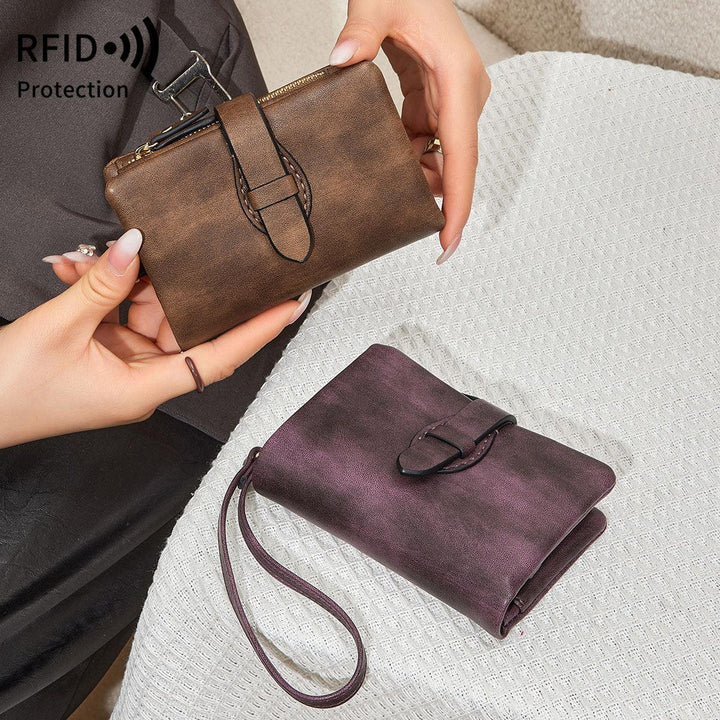 Hands holding a brown leather RFID protection wallet next to a purple leather wristlet wallet on white textured fabric