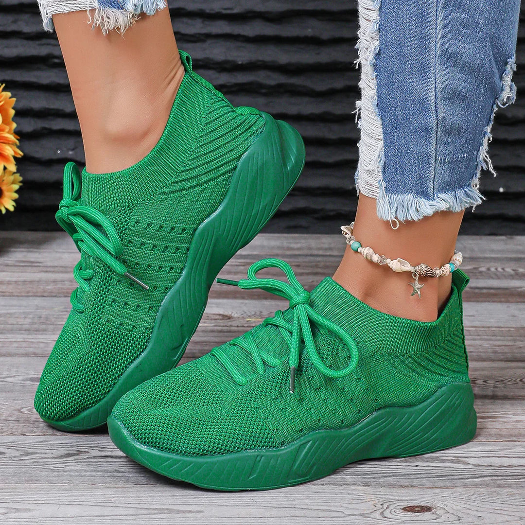 Green knit sneakers with thick soles worn with frayed blue jeans and seashell anklet on wooden floor