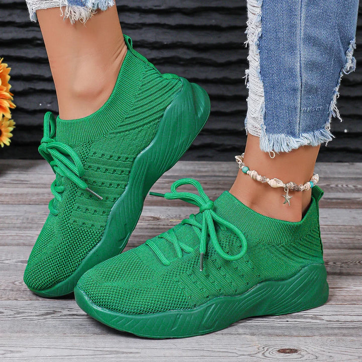 Green knit sneakers with thick soles worn with frayed blue jeans and seashell anklet on wooden floor