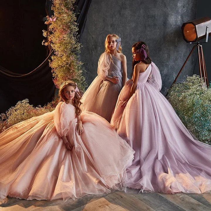 Three girls in elegant pastel pink and lavender tulle dresses posing with floral decorations and vintage spotlight