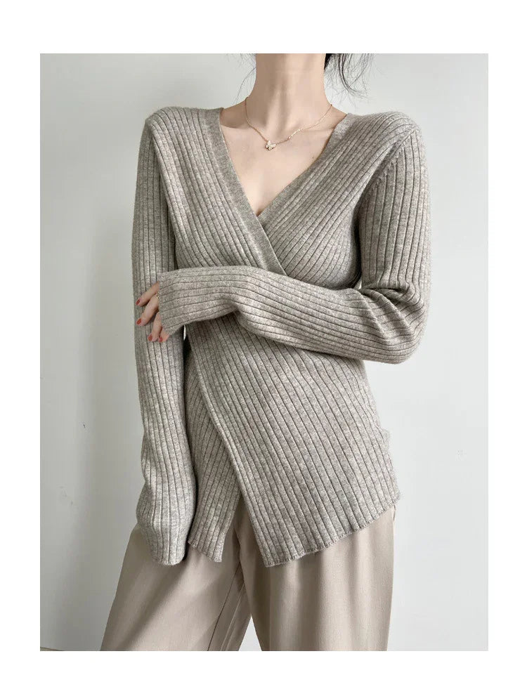 Woman wearing a beige ribbed knit wrap sweater with long sleeves and beige pants against a plain white background