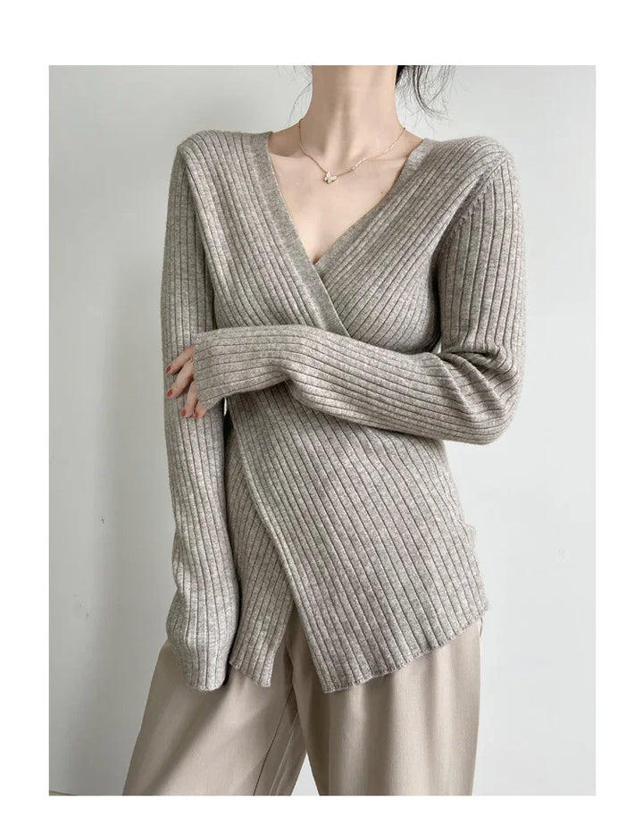 Woman wearing a beige ribbed knit wrap sweater with long sleeves and beige pants against a plain white background