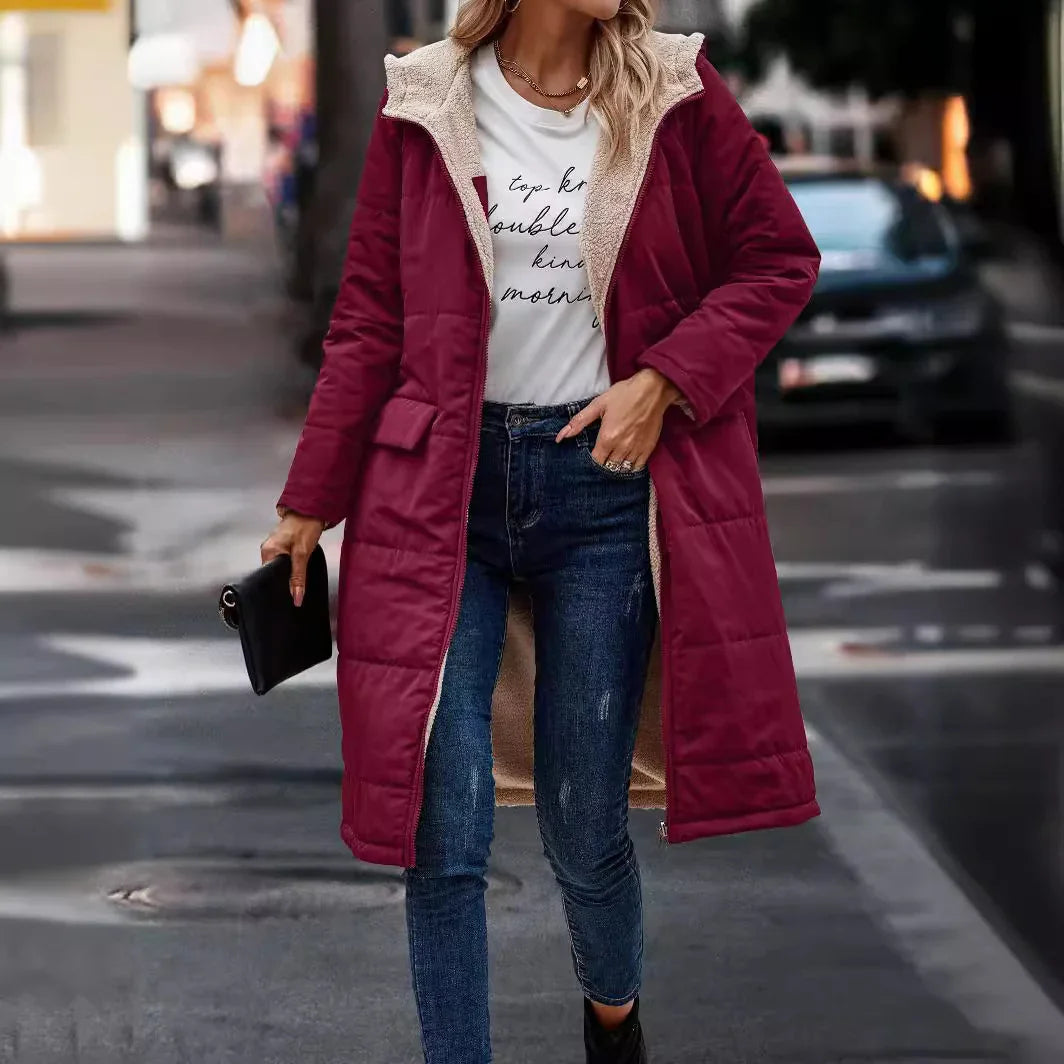 Woman wearing burgundy padded long coat with beige sherpa lining, white graphic tee, jeans, and carrying black clutch