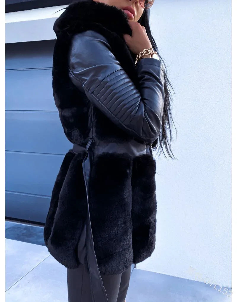 Woman wearing black faux fur vest with leather quilted sleeves and gold bracelet near white wall