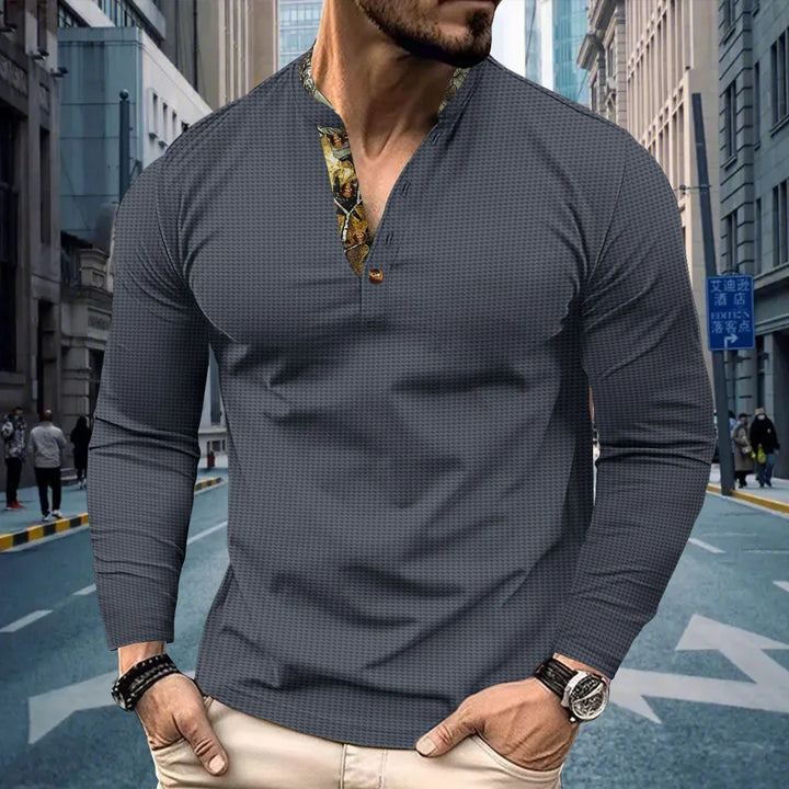 Man wearing dark textured long-sleeve Henley shirt with floral inner collar and beige pants in urban street setting