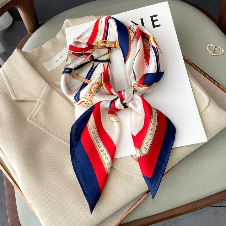 Red, white, and blue patterned silk scarf tied on beige coat with fashion magazine on gray chair
