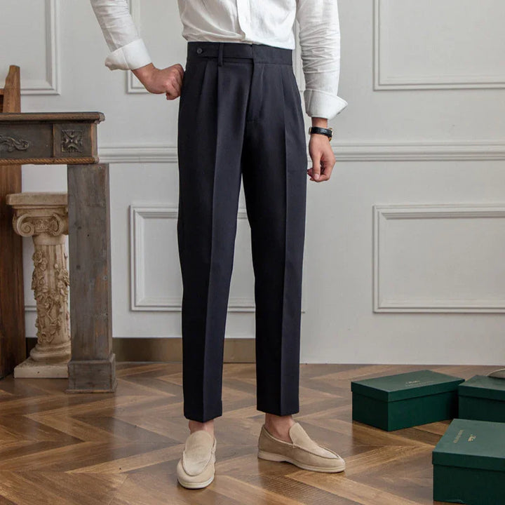 Man wearing black pleated trousers and beige loafers standing on wooden floor in elegant room