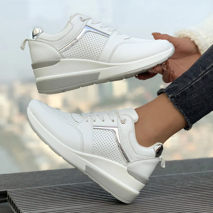 White perforated leather sneakers with silver accents worn by person in black jeans and fuzzy white jacket