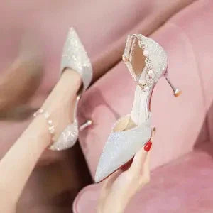 Elegant white high-heeled shoes with pearl and lace embellishments on pink velvet sofa