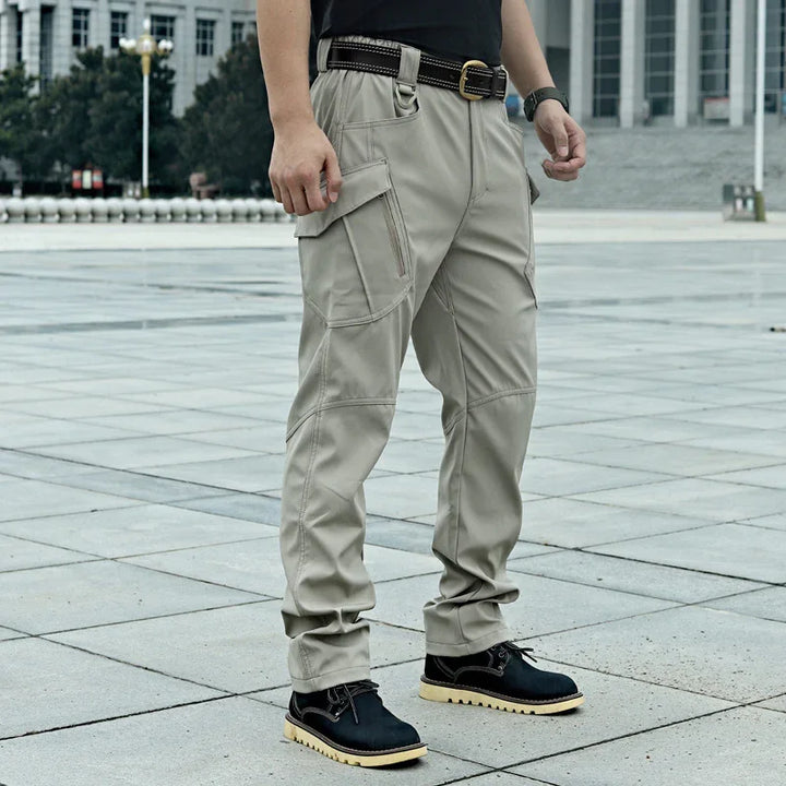 Man wearing beige tactical cargo pants with multiple pockets and black casual shoes on urban pavement