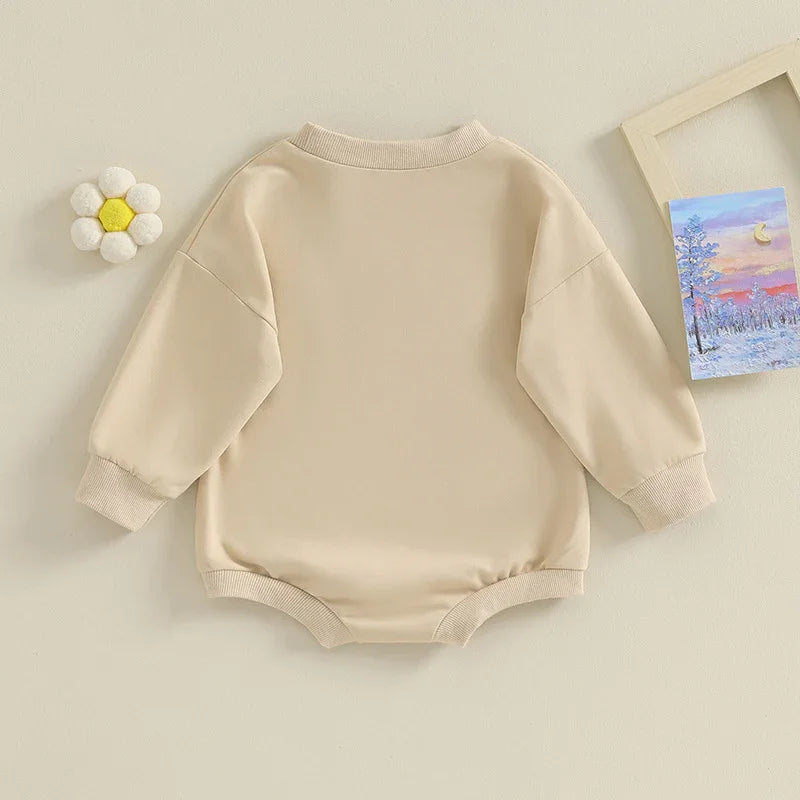 Beige long sleeve baby romper with ribbed cuffs and neckline laid flat on cream surface