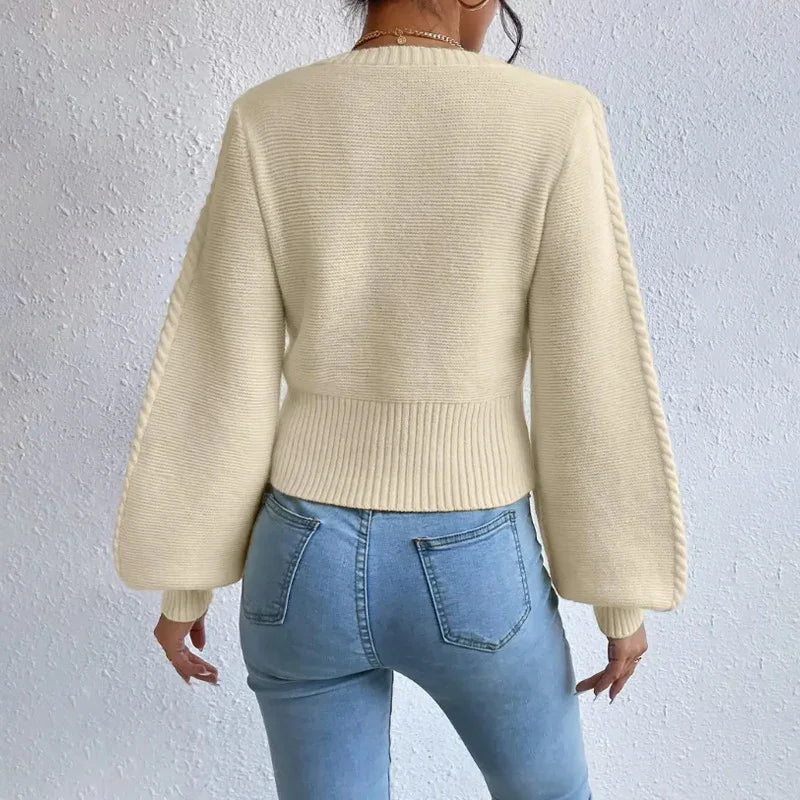 Woman wearing cream knit sweater with balloon sleeves and light blue high-waisted jeans against white wall