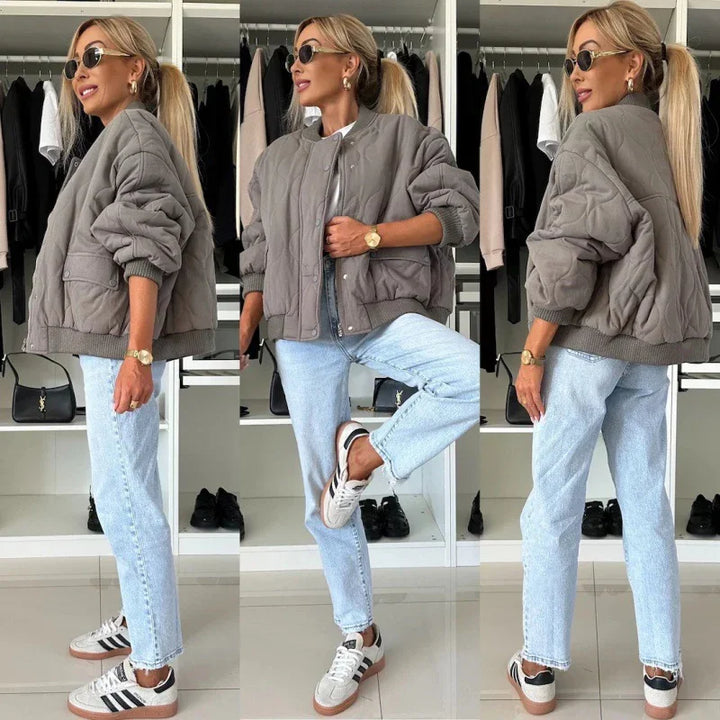 Woman wearing oversized quilted gray bomber jacket, light blue jeans, and Adidas sneakers in modern closet