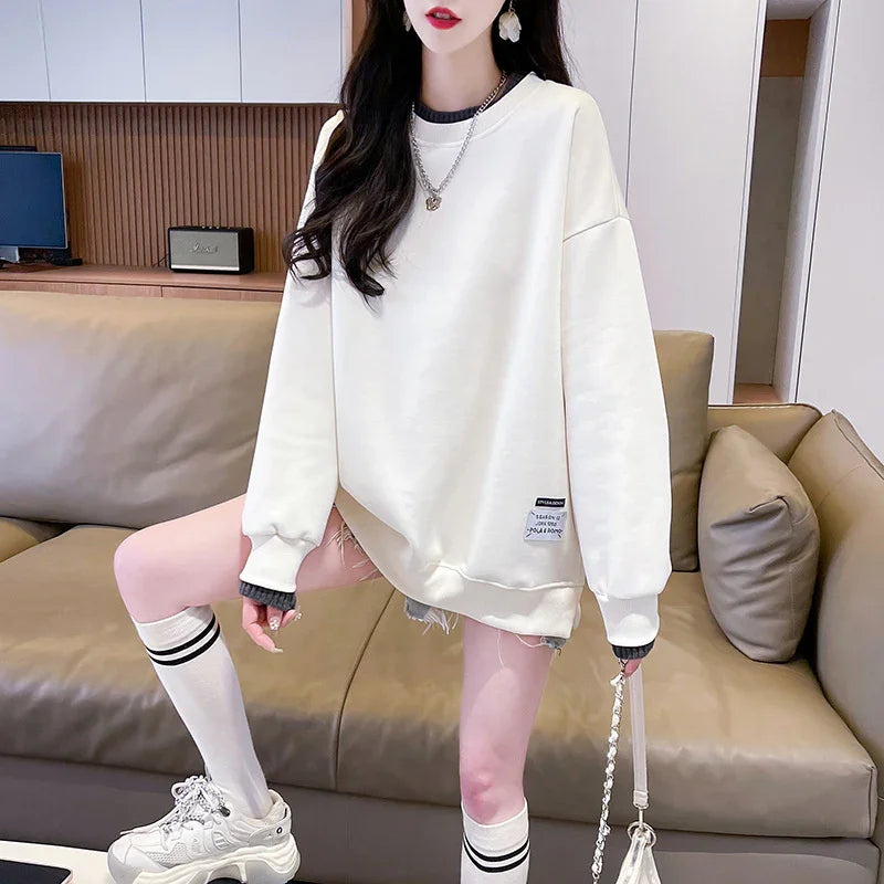 Woman wearing white oversized sweatshirt, denim shorts, knee-high sporty socks, and chunky sneakers sitting on beige leather sofa