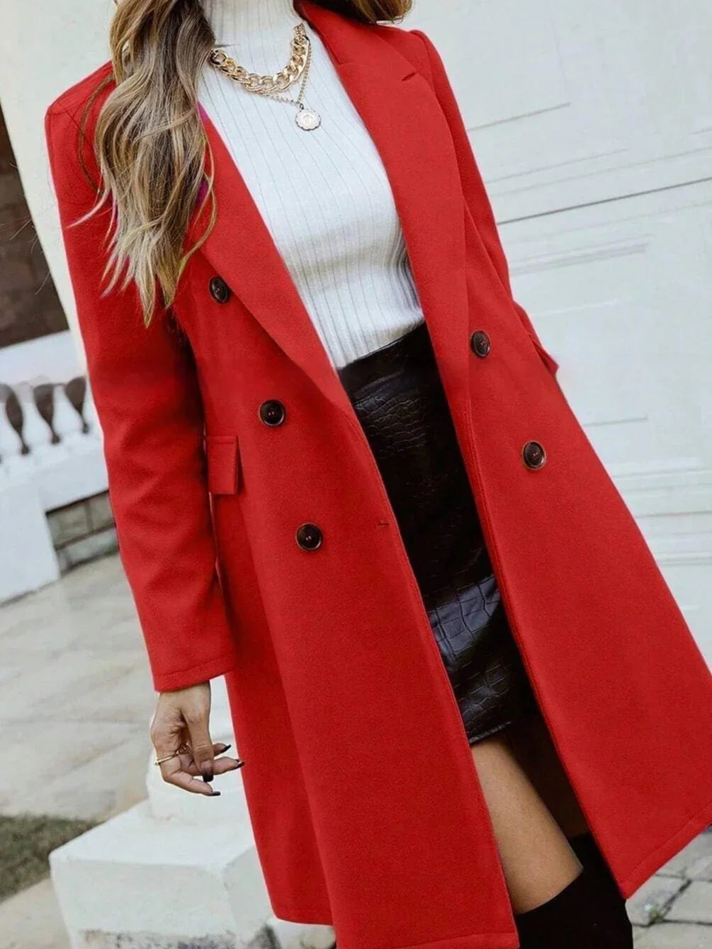 Woman wearing a red double-breasted coat, white ribbed turtleneck sweater, black leather skirt, and gold chain necklaces