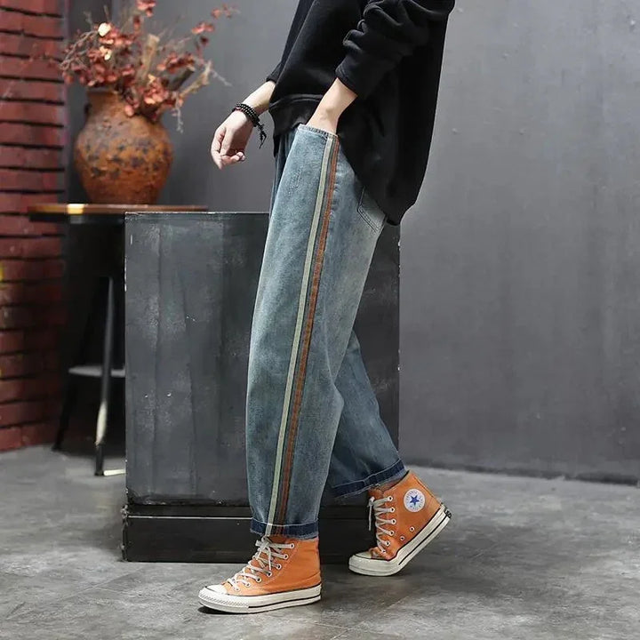 Person wearing blue denim jeans with side stripes and orange high-top sneakers in urban setting