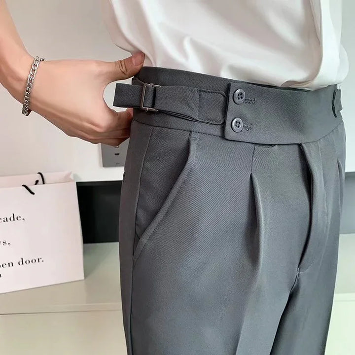 Close-up of gray pleated trousers with side adjuster and buttons worn with white shirt