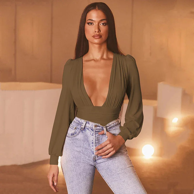 Woman wearing olive green deep V-neck blouse and high-waisted light blue jeans in warm-lit room