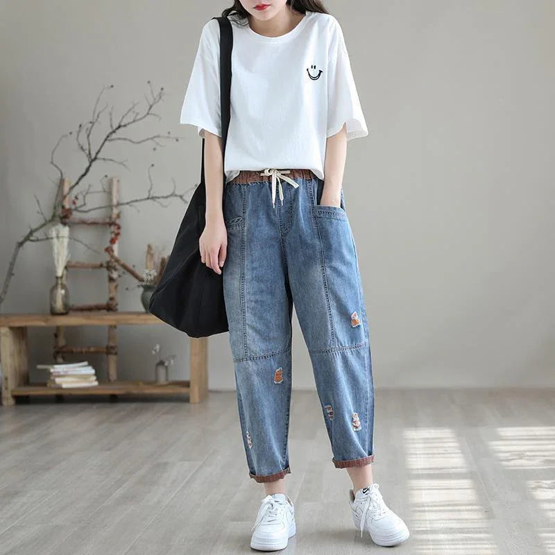 Casual outfit with white smiley face t-shirt, loose distressed denim pants, white sneakers, and black tote bag indoors