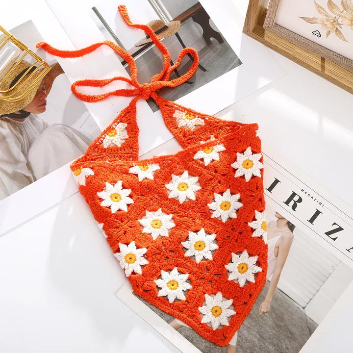Orange crochet halter top with white daisy flower pattern on a flat surface with magazines