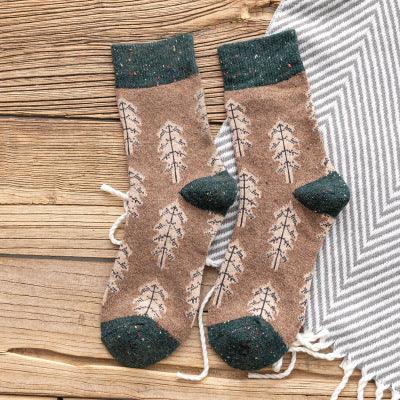 brown wool socks with tree patterns and dark green toes, heels, and cuffs on wooden surface next to grey and white striped fabric