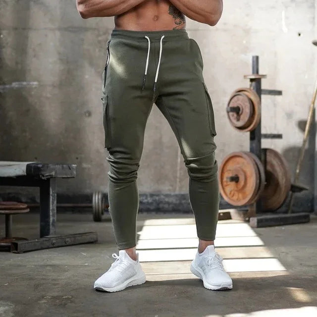 Man wearing olive green cargo jogger pants and white sneakers in gym with weightlifting equipment