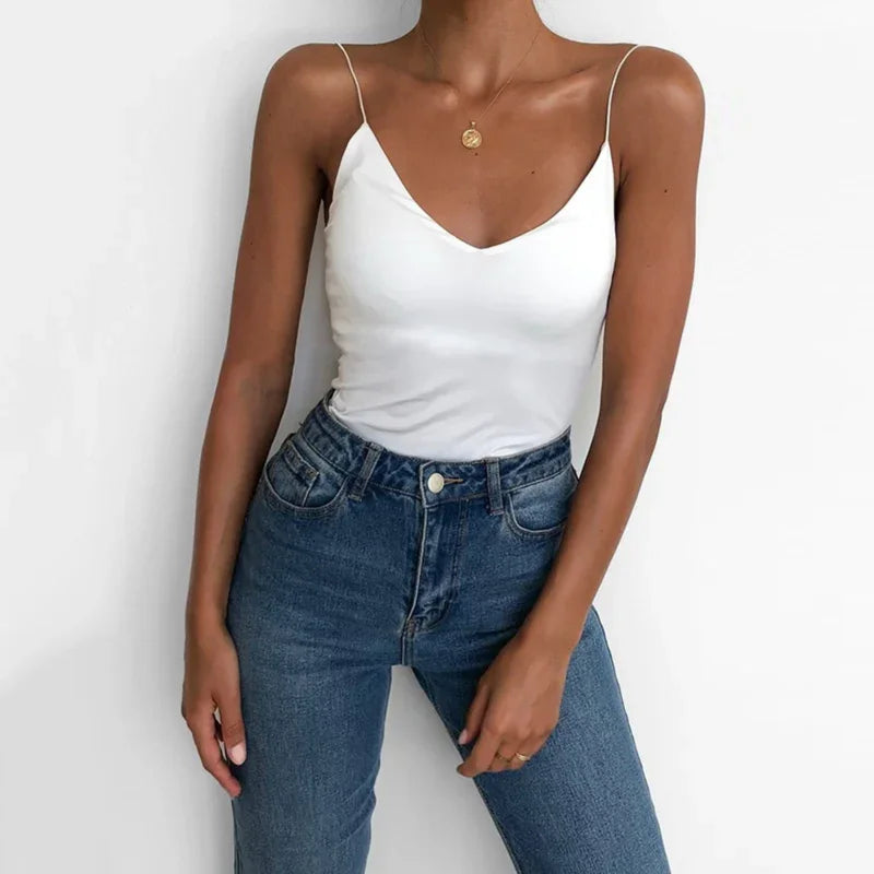 Woman wearing white spaghetti strap tank top and high-waisted blue jeans against white background