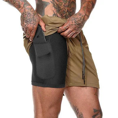 Tattooed man wearing khaki shorts with black inner compression shorts featuring a side pocket holding a phone
