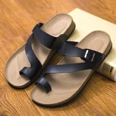 Pair of brown sandals with black leather straps and toe loop on wooden surface