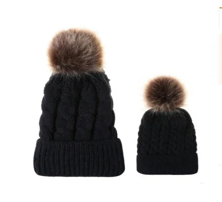 Two black knitted winter hats with brown faux fur pom-poms, one adult size and one baby size