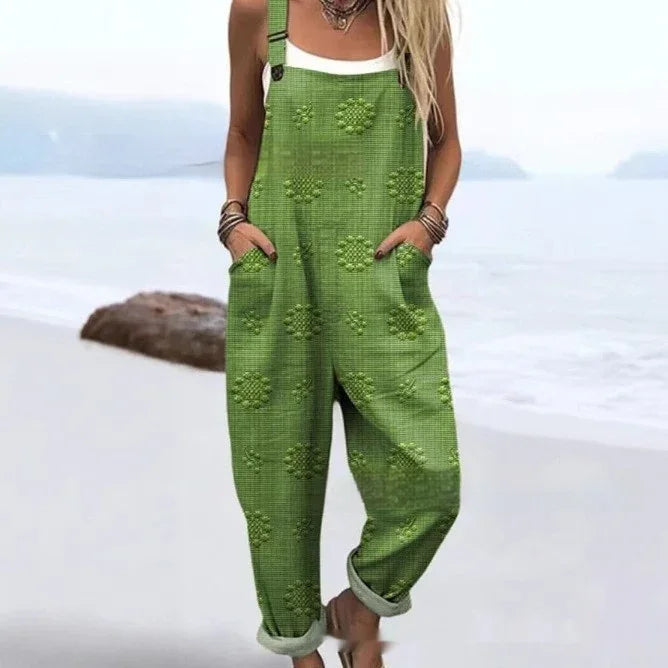 Woman wearing green floral textured overalls with rolled cuffs and white tank top on the beach