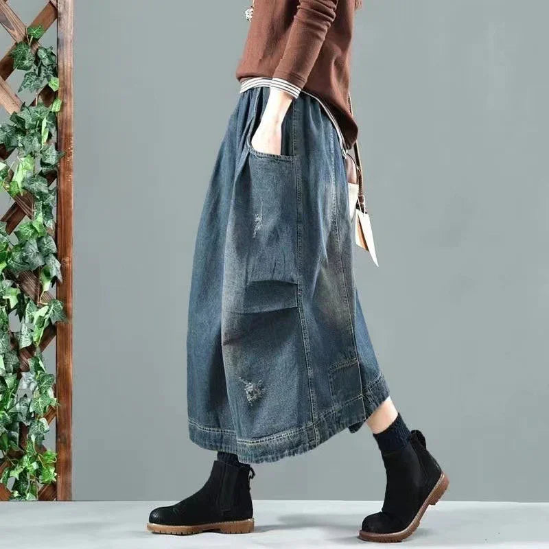 Woman wearing distressed denim midi skirt with pockets and black ankle boots against gray background