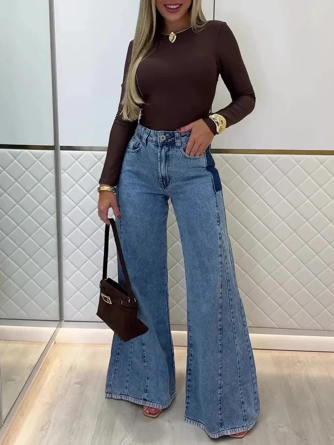 Woman wearing brown long-sleeve top and high-waisted wide-leg jeans holding small brown handbag