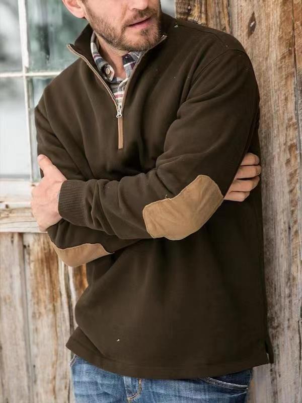 Man wearing a brown quarter-zip pullover with tan elbow patches and plaid shirt, rustic wooden background