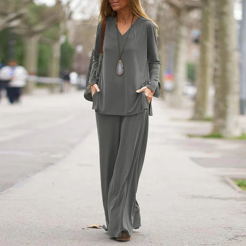 Woman walking outdoors wearing gray loose-fit long sleeve top and wide-leg pants outfit with pendant necklace