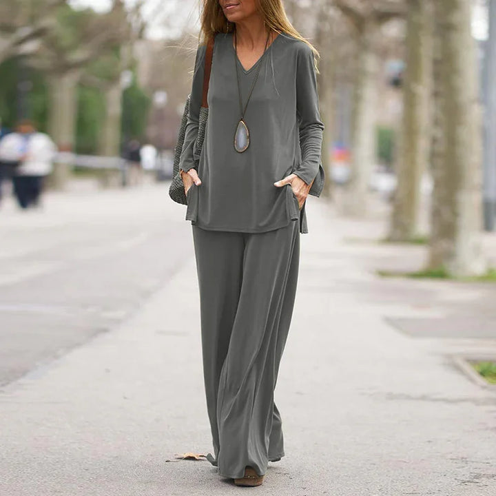 Woman walking on sidewalk wearing a stylish gray long-sleeve top and wide-leg pants outfit with pendant necklace