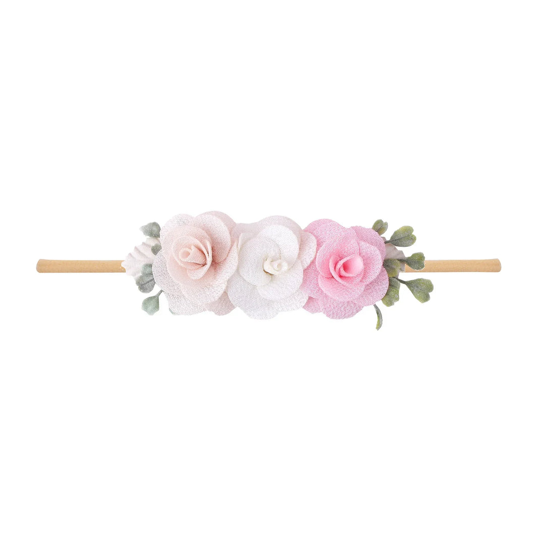 Delicate headband with three fabric flowers in blush, white, and pink on a light brown band