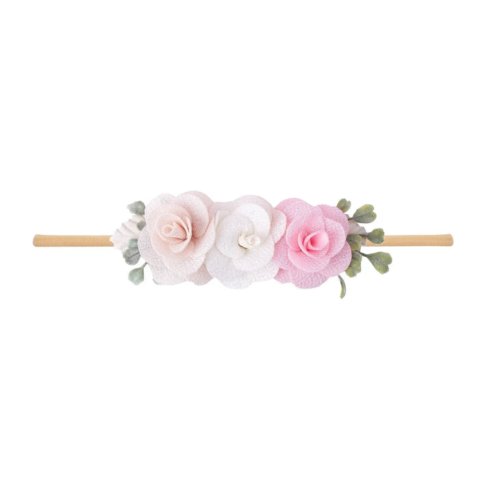 Delicate headband with three fabric flowers in blush, white, and pink on a light brown band