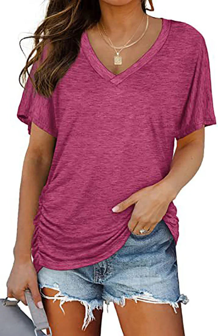 Woman wearing a raspberry pink V-neck t-shirt and distressed denim shorts holding a gray bag
