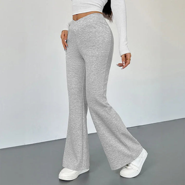 Woman wearing high-waisted light gray flare pants with white sneakers and white cropped long-sleeve top