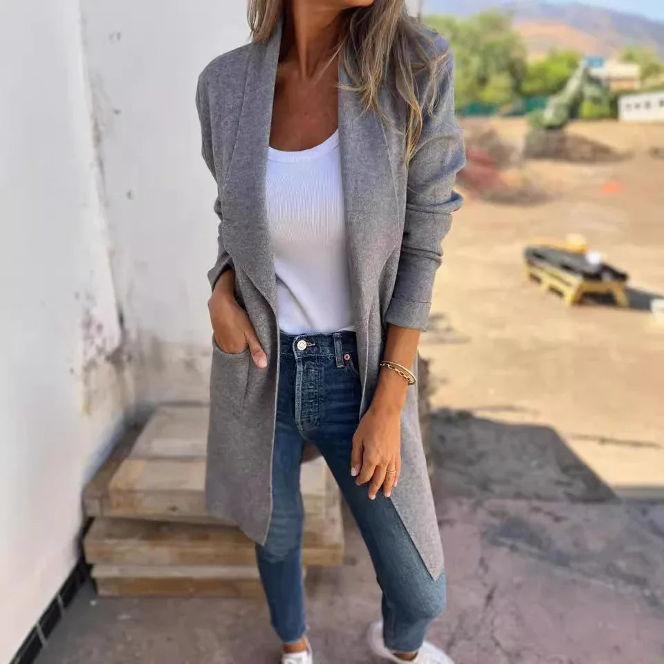 Woman wearing gray open cardigan, white tank top, blue jeans, and white sneakers outdoors