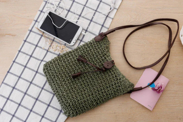 Green crocheted shoulder bag with brown strap on wooden surface next to smartphone and pink notebook