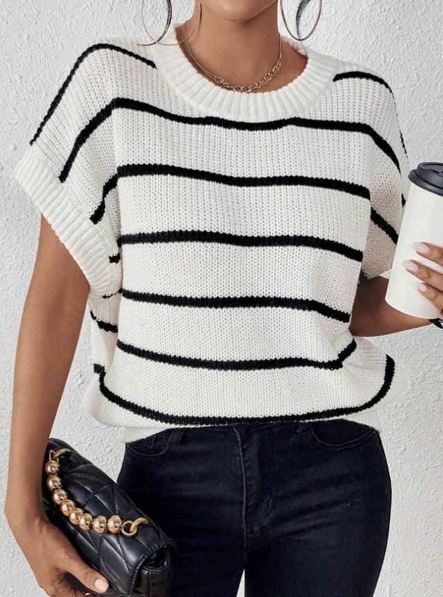 Woman wearing white and black striped knit sleeveless top with black jeans, holding black quilted purse and coffee cup