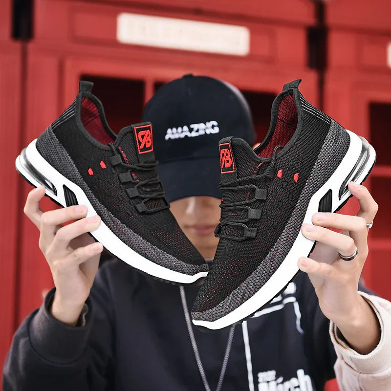 Person holding black and gray knit athletic shoes with white soles and red accents in front of red background